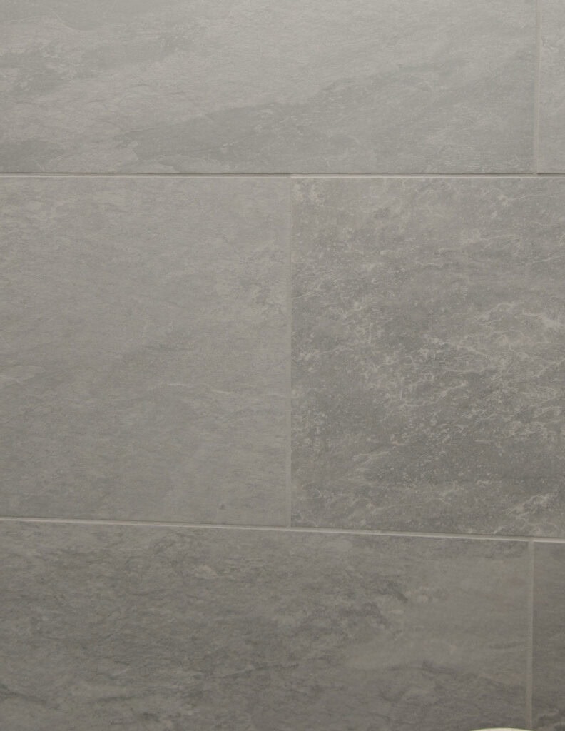 Close-up of a wall covered with rectangular grey tiles that have a slightly textured, stone-like surface and subtle color variations.