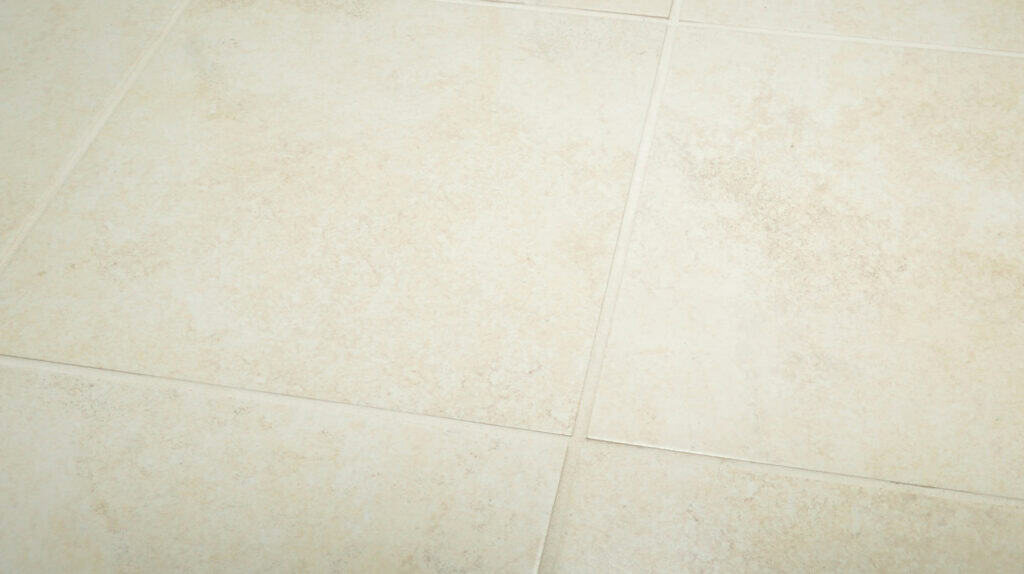 Beige ceramic floor tiles with a subtle mottled texture and visible grout lines, arranged in a grid pattern.