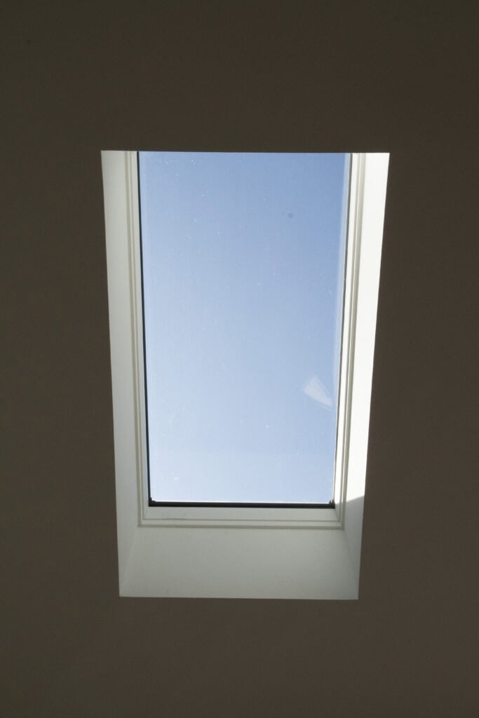 A rectangular skylight window set in a white ceiling, showing clear blue sky through the glass.