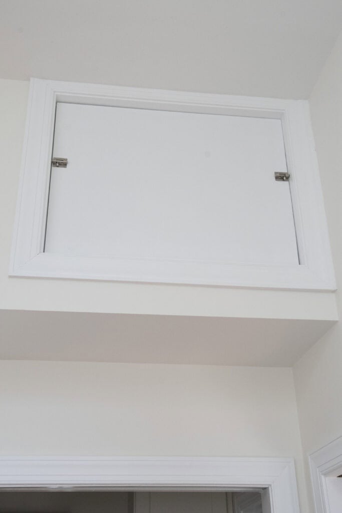 A small white door with two hinges is set high on a wall above an entryway, likely serving as an attic or storage access panel.