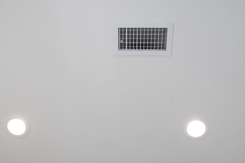 A white ceiling with two round recessed lights and a rectangular air vent in the center.
