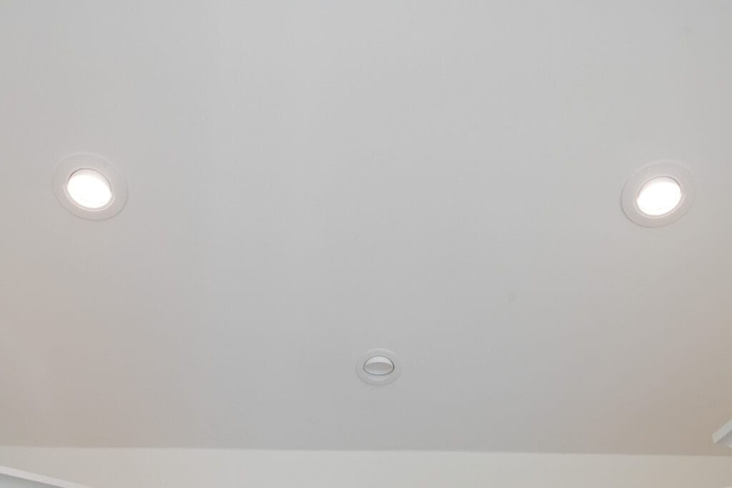 A white ceiling with three fixtures: two round, recessed lights on either side and a small circular vent or smoke detector in the center.