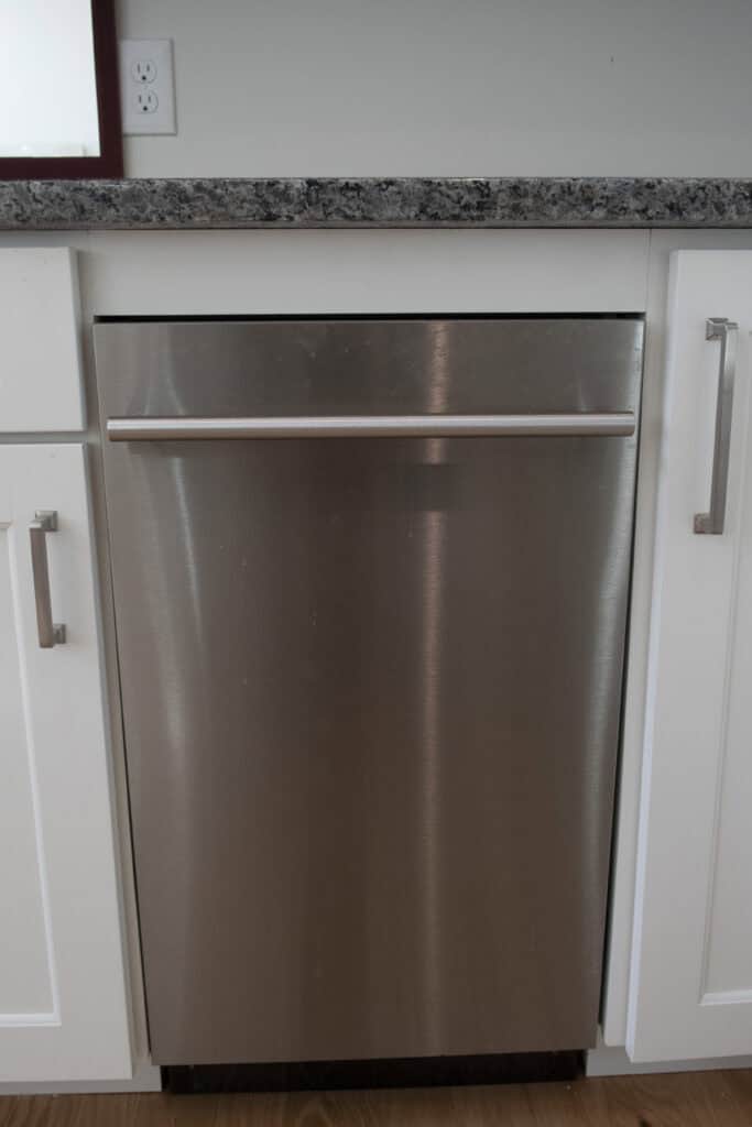 A stainless steel dishwasher is built into white cabinetry beneath a gray granite countertop in a modern kitchen.