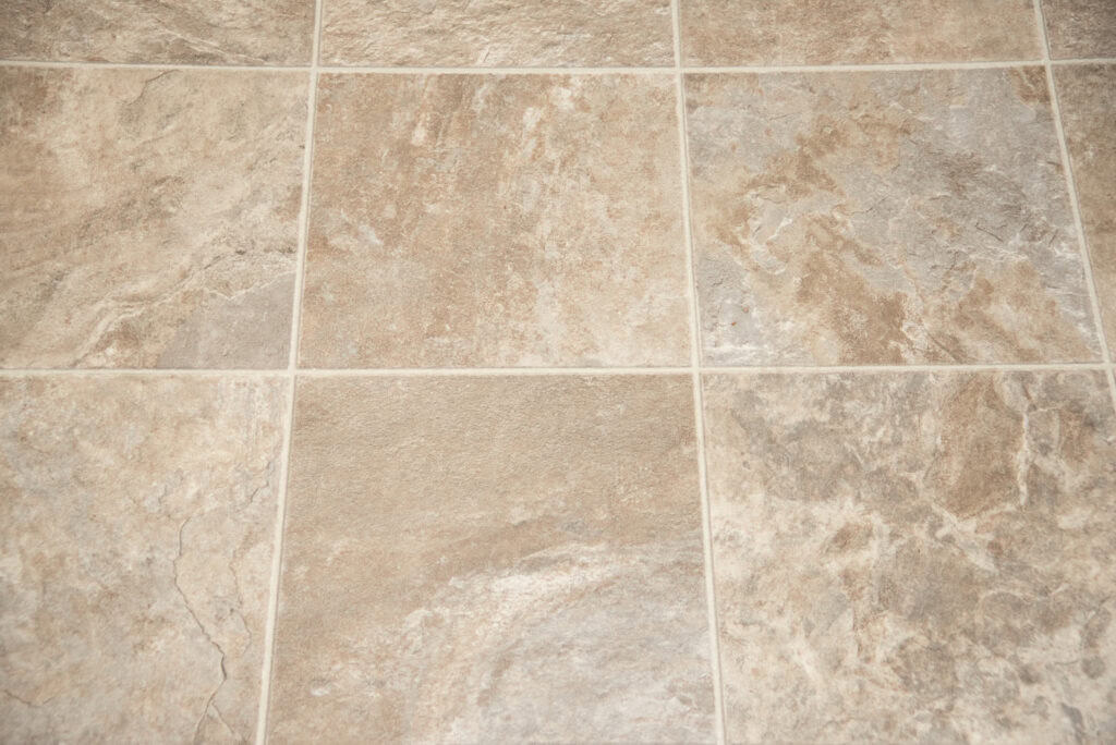 Close-up view of beige and light gray ceramic tiles with a textured, stone-like pattern. The tiles are arranged in a grid with visible grout lines.