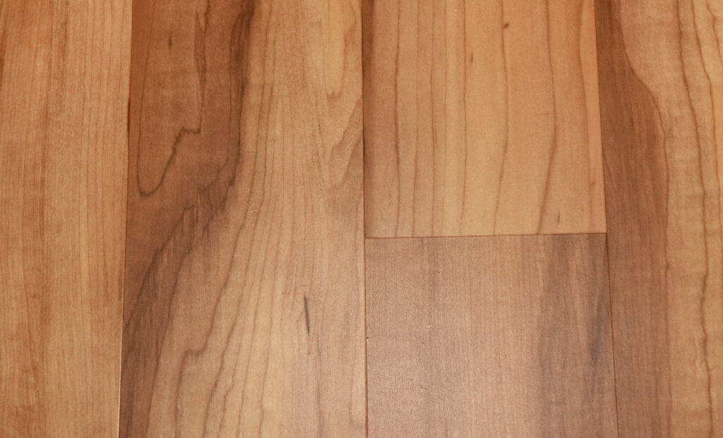 Close-up of a light brown wooden floor with visible natural grain patterns and slight color variations in each plank.