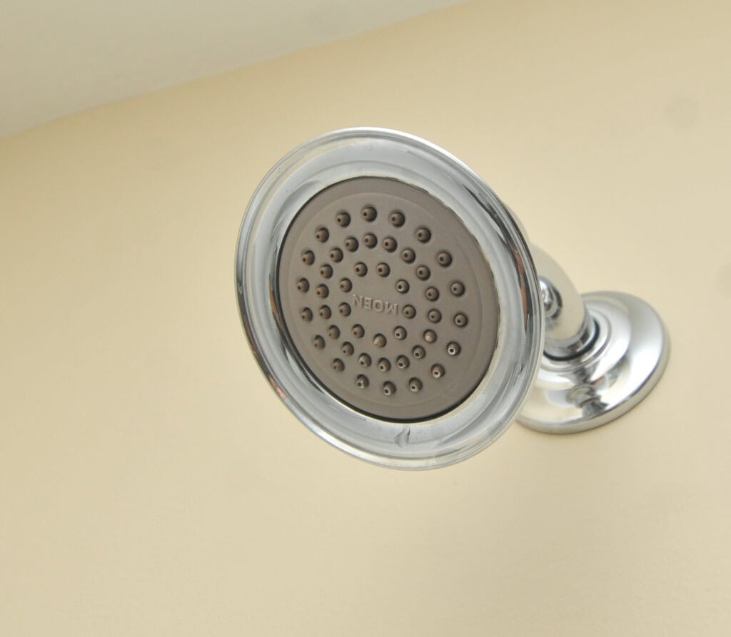 A close-up of a chrome showerhead mounted on a wall, with multiple small water nozzles and the word “ON/OFF” visible in the center. The background is a plain beige wall.