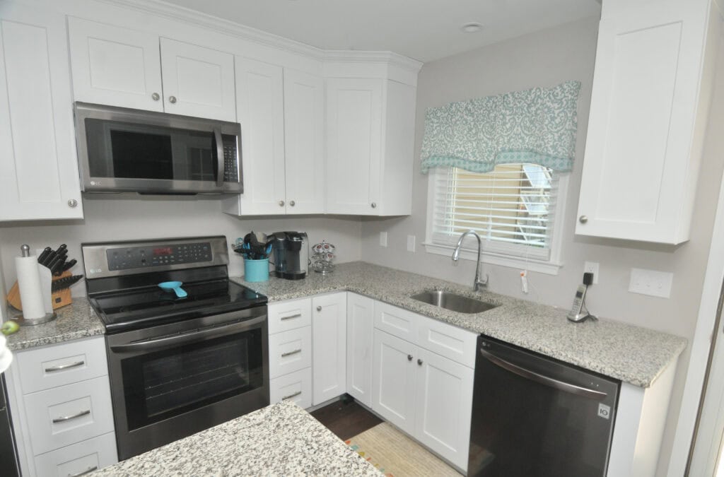 Modern kitchen with white cabinets, granite countertops, stainless steel appliances, a coffee maker, knife block, and a window above the sink with a blue patterned valance. The kitchen has a clean and organized look.