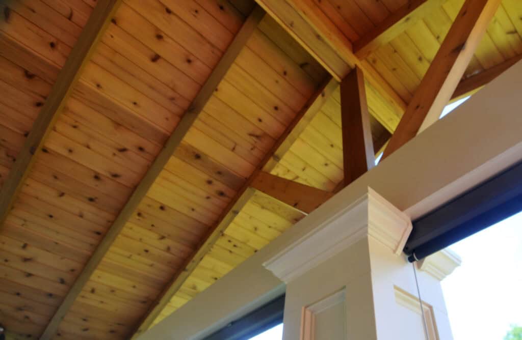 View looking up at a wooden ceiling with exposed beams and a decorative white column in the foreground, showing natural wood textures and architectural details.