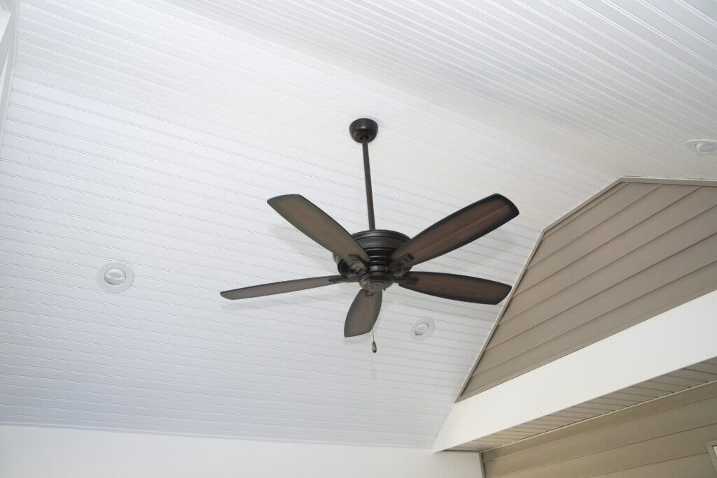 A dark ceiling fan with five blades hangs from a white, paneled ceiling with recessed lights; part of a beige wall is visible in the corner.