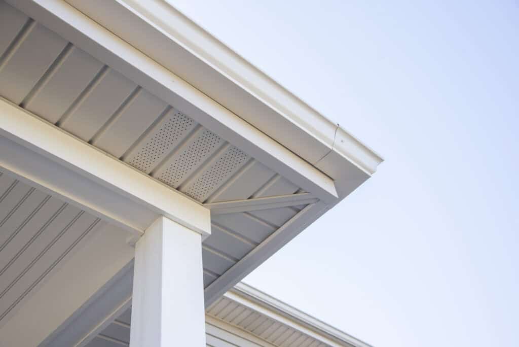 Close-up view of the corner of a house roof showing white soffit, fascia, gutter, and supporting column against a clear blue sky.