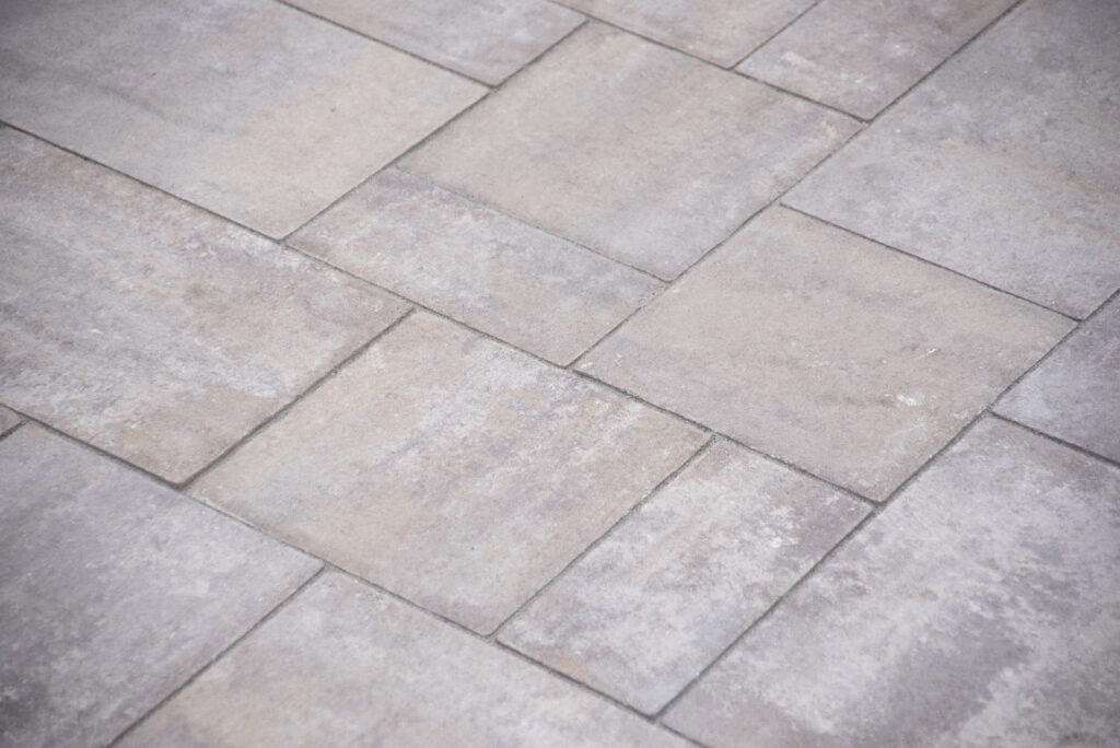 Light gray stone pavers arranged in a staggered rectangular pattern, creating a textured and uniform surface, often used for patios or walkways.