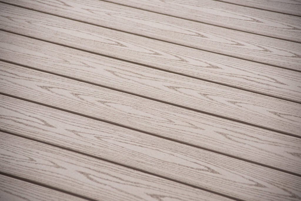 Light-colored wooden deck boards arranged horizontally, featuring a subtle wood grain pattern and evenly spaced grooves between each board. The surface appears clean and well-maintained.