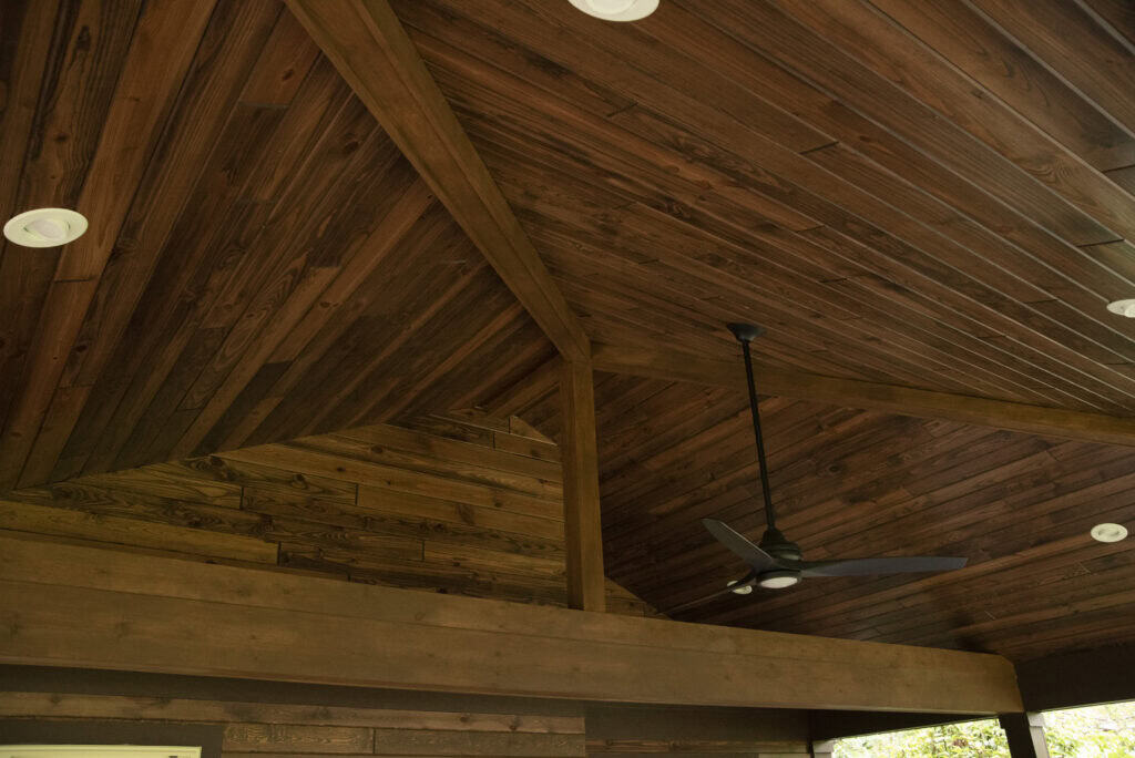 A ceiling made of dark wooden planks in a geometric pattern, featuring recessed ceiling lights and a modern black ceiling fan.