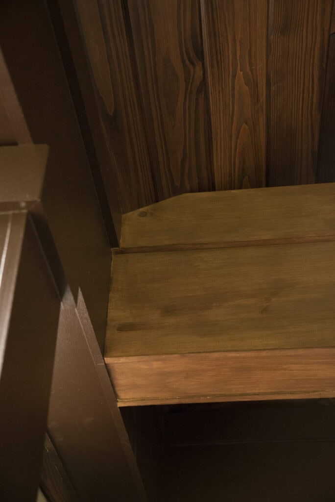 A close-up view of a wooden ceiling with visible grain patterns and beams, featuring rich brown tones and natural textures.
