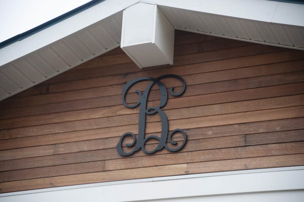 A large decorative black letter B is mounted on the wooden siding of a house gable, under the roofs white eaves.