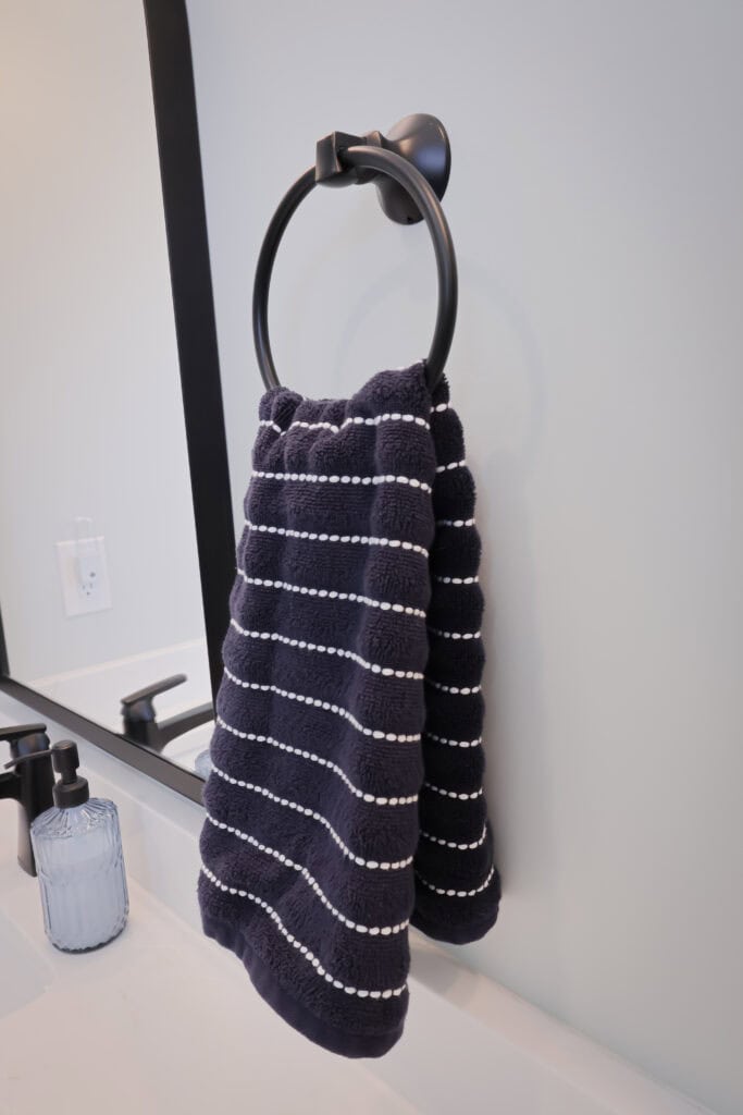 A dark blue towel with white horizontal stripes hangs on a black towel ring near a bathroom sink with a soap dispenser and a mirror.