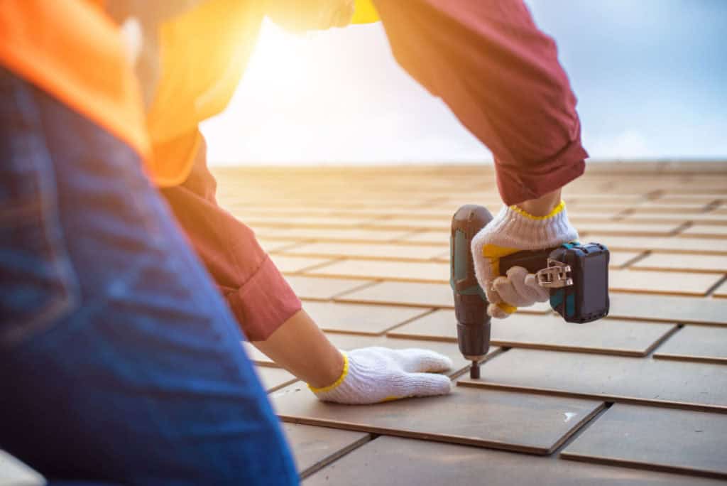 A person wearing gloves using a drill to install a roof.