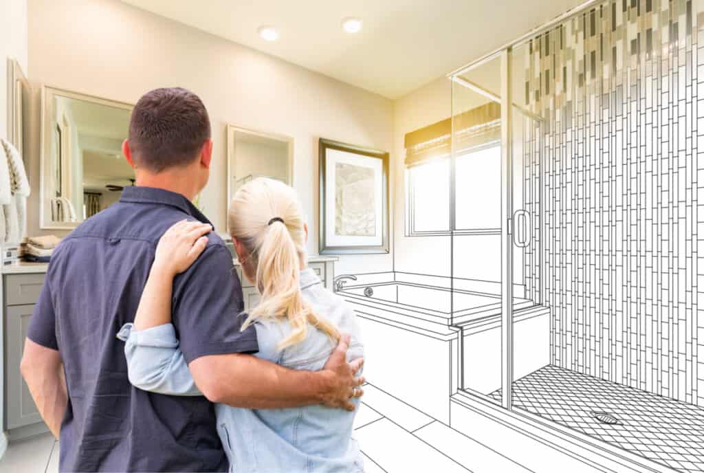 A couple stands in a bathroom, looking at a partially completed digital illustration of a remodeled shower and tub area merged with the existing room.