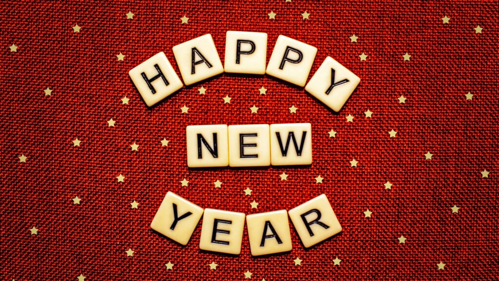 Scrabble tiles spell “HAPPY NEW YEAR” on a red textured background decorated with small gold stars, hinting at festive 2025 Renovation Trends for a sparkling celebration.