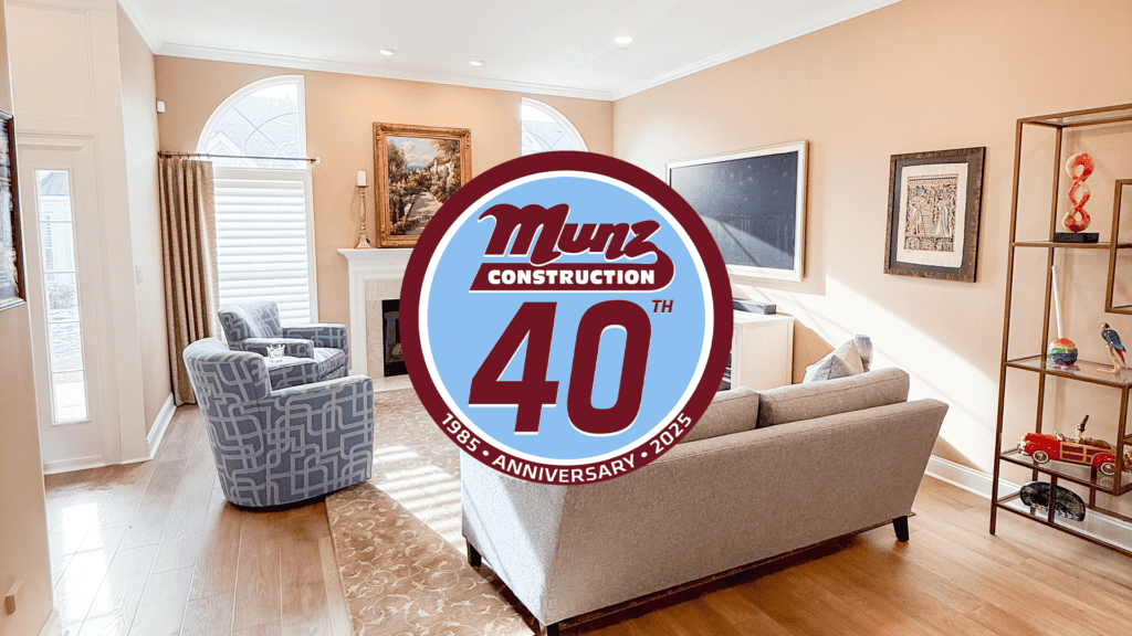 A bright, modern living room with two sofas, armchairs, art on the walls, and large windows invites you to expand your space. A Munz Construction 40th Anniversary 1985-2025 logo is centered over the image.