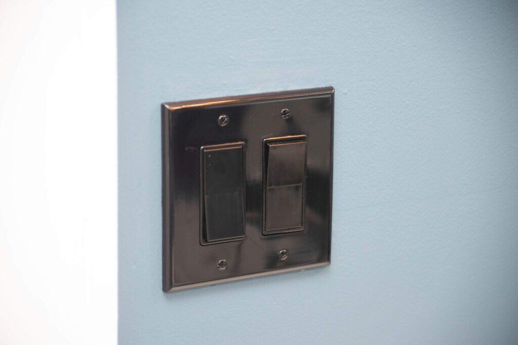 A close-up of a metallic double light switch plate with two rectangular switches mounted on a blue wall next to a white corner.