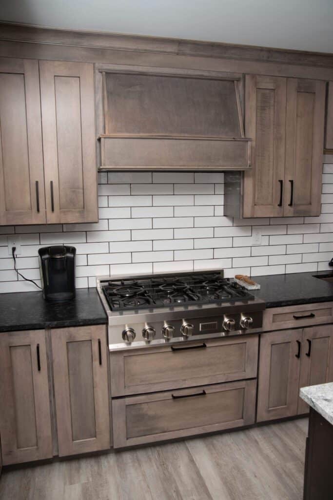Modern kitchen with wooden cabinets, black countertops, a stainless steel gas stove, a range hood, a coffee maker, and white subway tile backsplash. The floor is light wood.