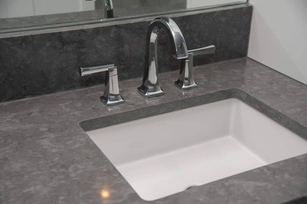 A modern bathroom sink with a rectangular white basin, gray marble countertop, chrome faucet, and handles, with a mirror in the background.