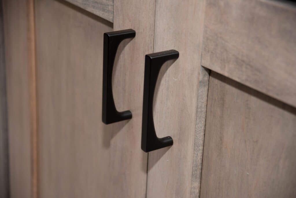 Close-up of two black metal handles on light-colored wooden cabinet doors.