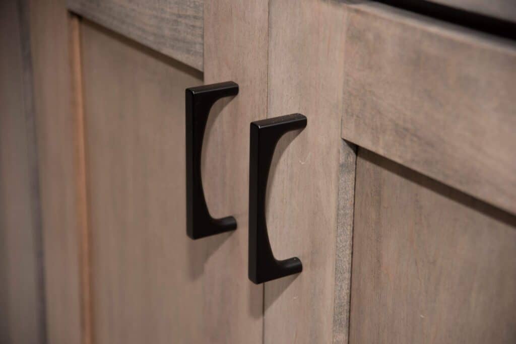 Close-up of two black metal handles on light wood cabinet doors with a natural grain pattern.