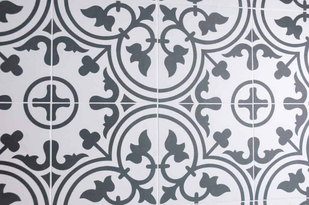 Black and white ceramic tiles with intricate, symmetrical floral and geometric patterns create a repeating decorative design. The tile grout lines form a grid.
