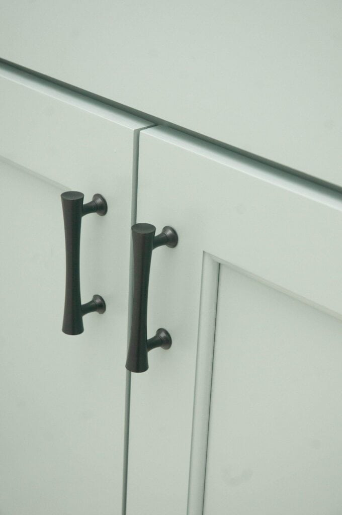 Close-up of two black metal handles on light-colored cabinet doors, showing a simple, modern design with clean lines and minimal detailing.