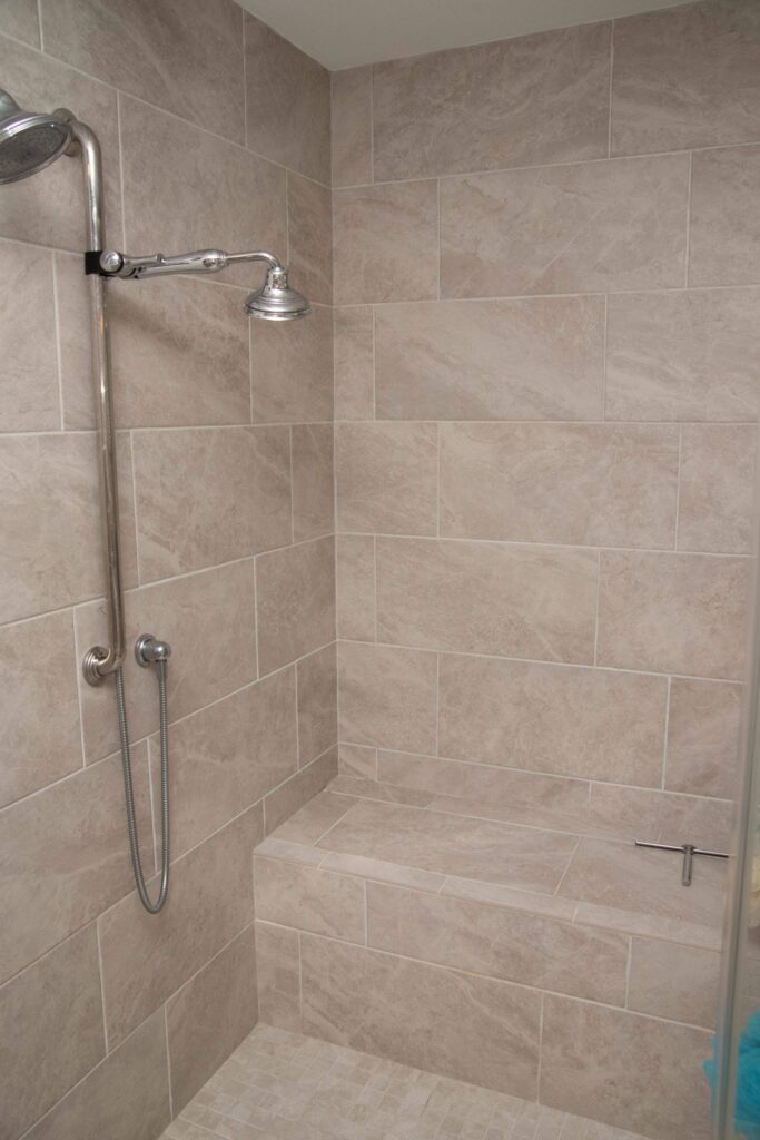 A tiled shower with beige tiles, a wall-mounted showerhead, a handheld shower, and a built-in bench. The shower is clean and modern with a rectangular layout.