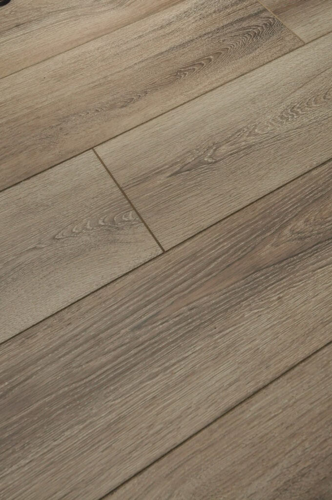 Close-up view of wooden floor panels with a natural, light brown grain pattern and subtle texture, arranged in a staggered layout.