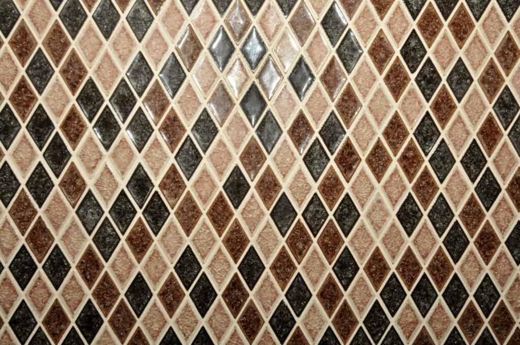 A close-up of a tiled surface with a repeating diamond pattern in shades of brown, beige, and black, creating a geometric, textured mosaic design.