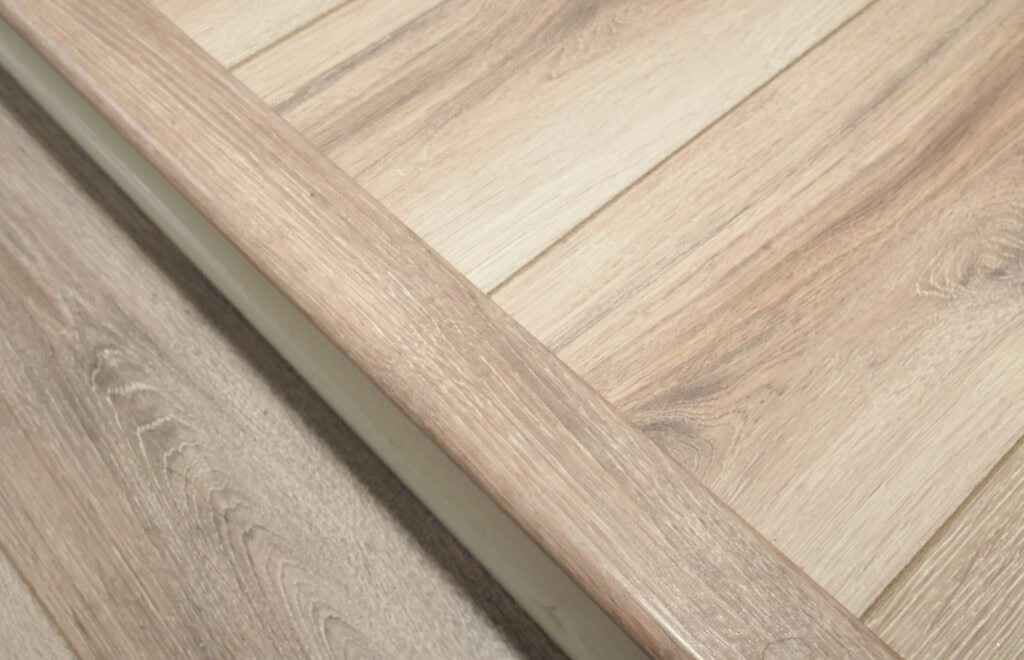 Close-up of light wood surfaces with distinct grain patterns, including a panel and a trim piece set at an angle, highlighting the texture and natural color variations of the wood.