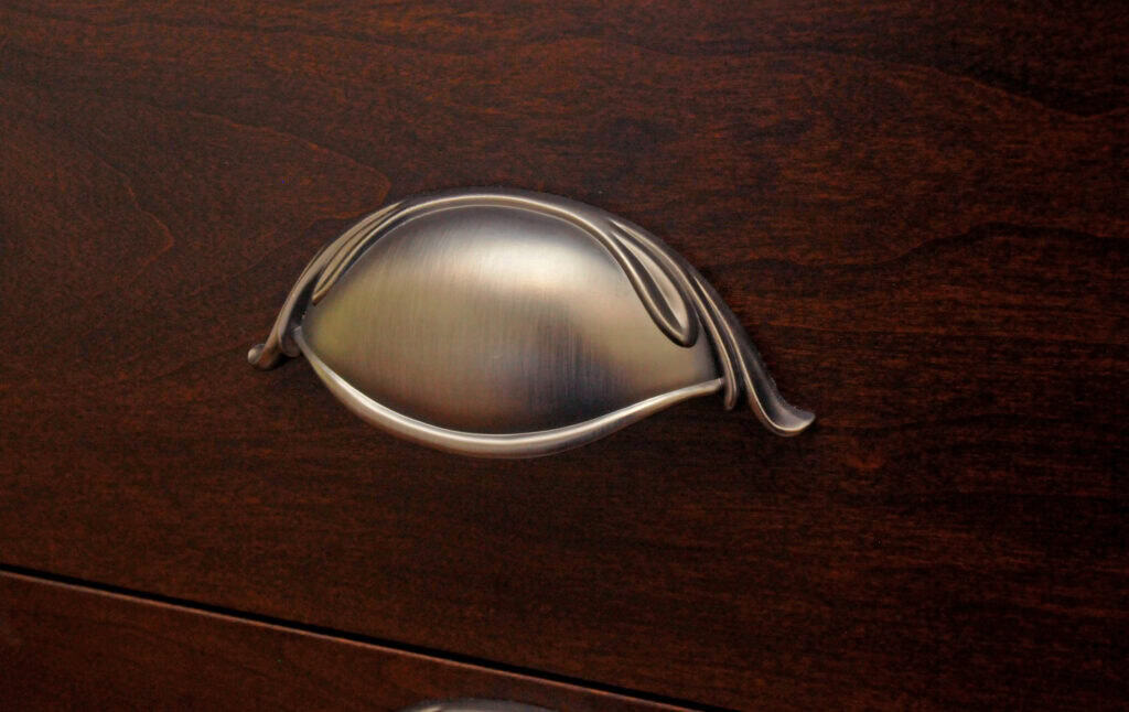 Brushed metal drawer handle with an elegant, curved design, mounted on a dark wood surface.