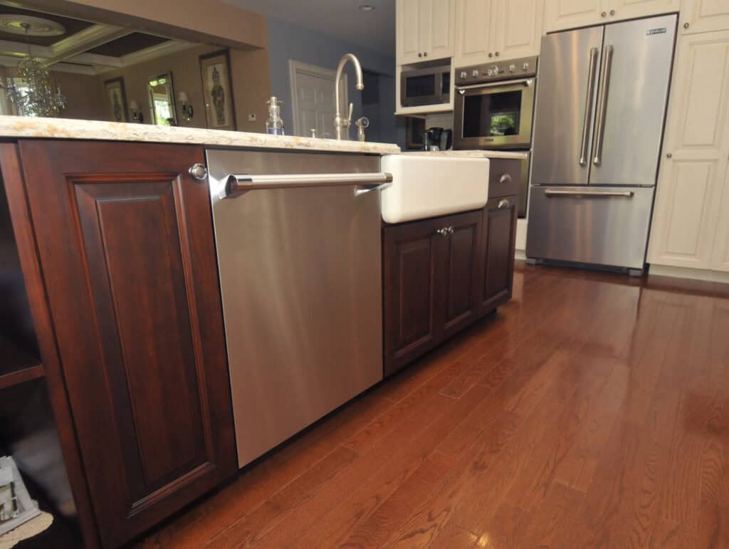 Modern kitchen with wooden cabinets, stainless steel dishwasher, farmhouse sink, and stainless steel refrigerator. Light countertops and wooden floor create a warm, inviting atmosphere.