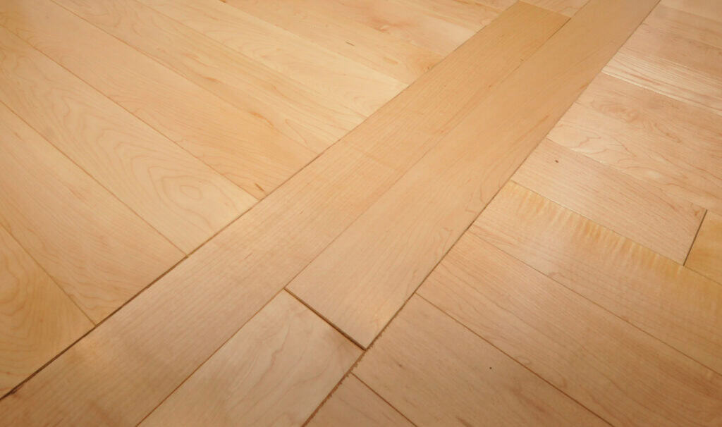 Light-colored wooden floorboards with two planks placed diagonally on top of the installed flooring, highlighting the unfinished or ongoing installation process.