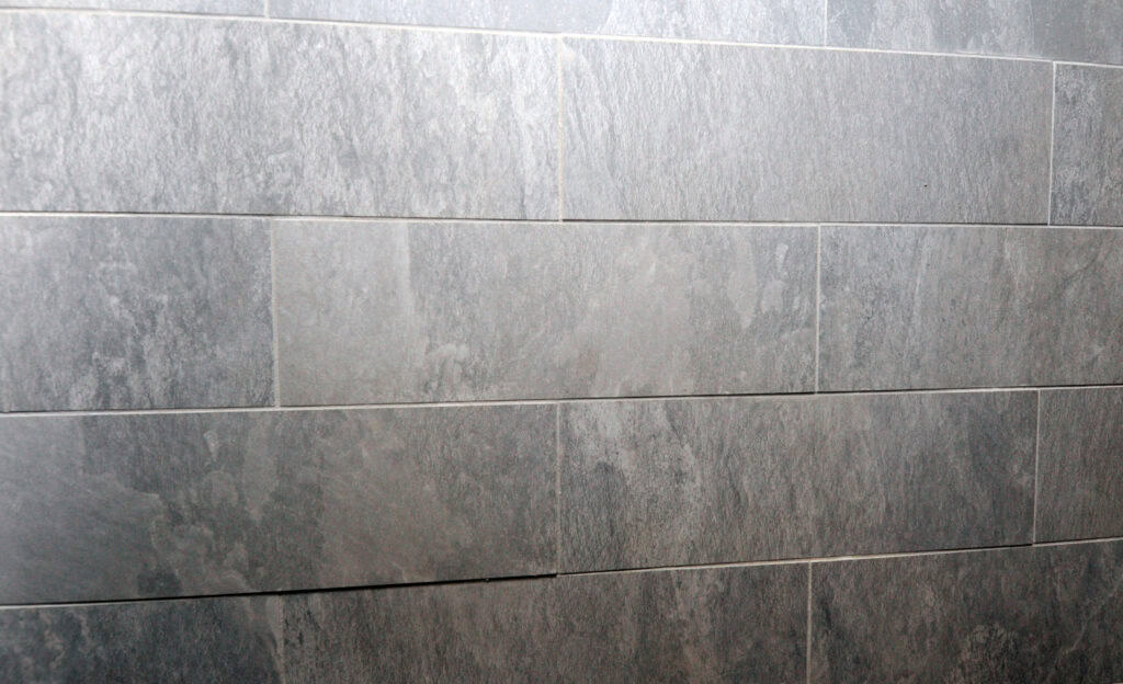 A close-up view of a wall covered with rectangular, gray stone tiles arranged in a horizontal, brick-like pattern. The tiles have a slightly textured and varied surface.