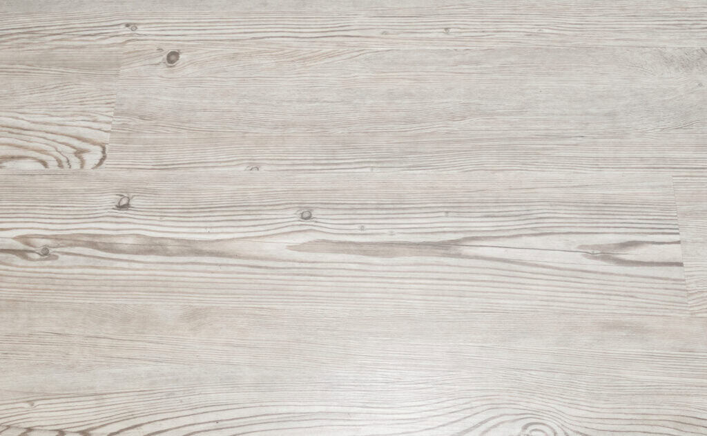 Light-colored wooden floor with a natural grain pattern and visible knots. The surface appears smooth and evenly finished, with horizontal lines accentuating the texture of the wood.