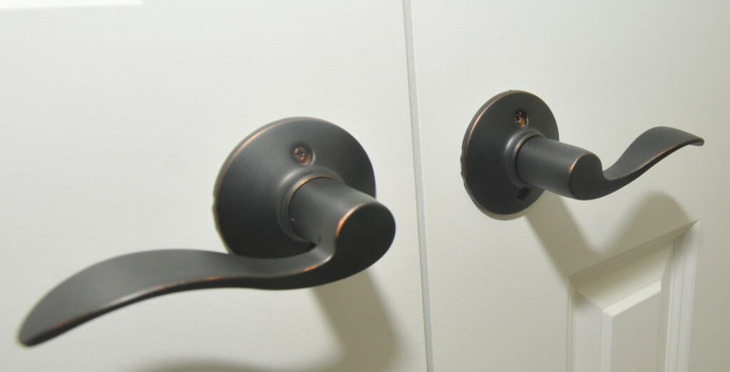 Two black metal door handles with curved levers are installed on white double doors, positioned side by side.