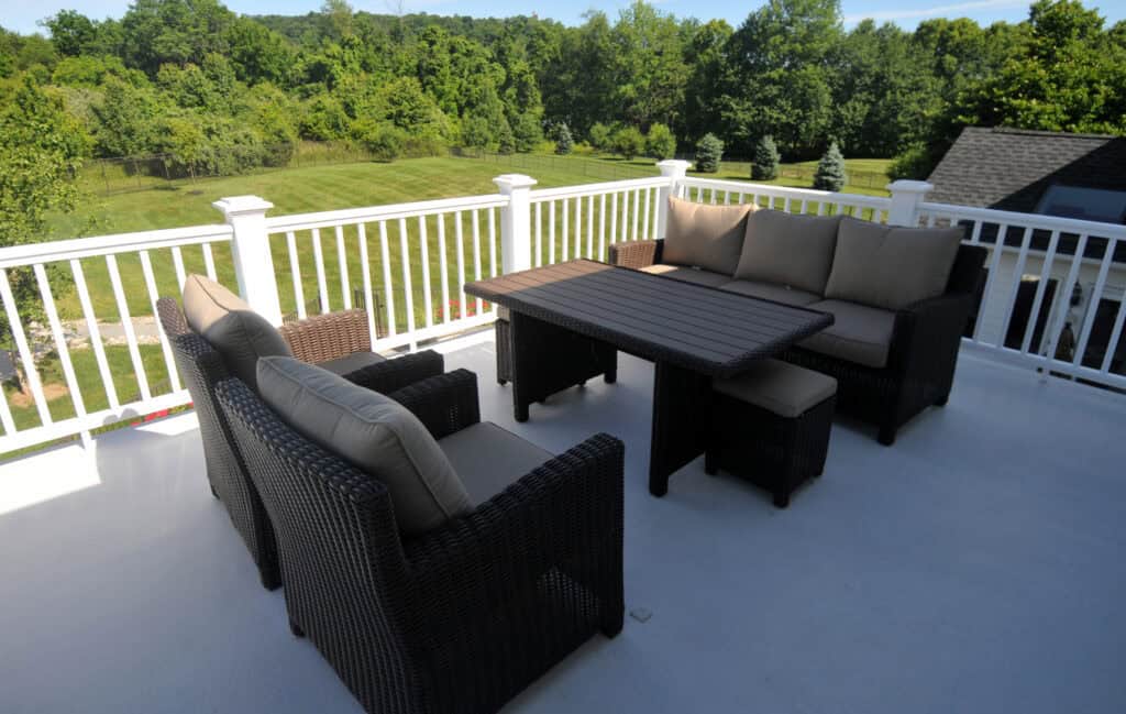 Outdoor patio set with a wicker sofa, two armchairs, and a rectangular table arranged on a white balcony, overlooking a grassy lawn and trees in the background.