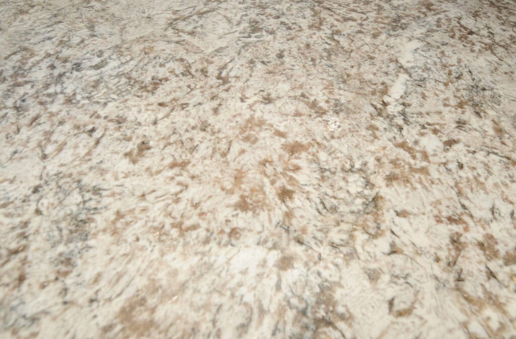 Close-up of a light-colored granite countertop surface with a mix of beige, brown, gray, and white tones, featuring natural, swirling stone patterns and textures.