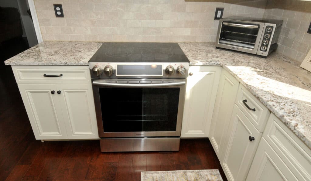 A modern kitchen with white cabinets, granite countertops, an electric stove with a glass cooktop, and a small stainless steel toaster oven on the right countertop.