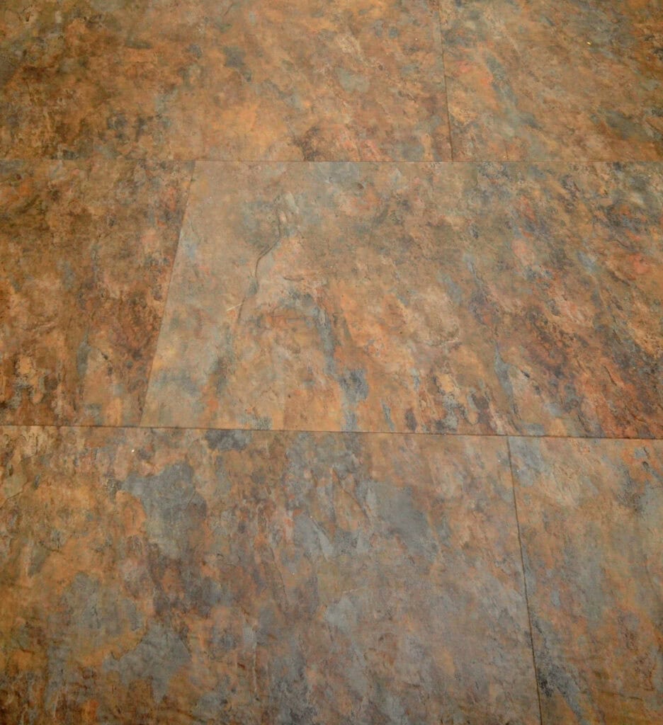 A close-up view of a brown and gray textured stone tile floor with irregular patterns and natural color variations.