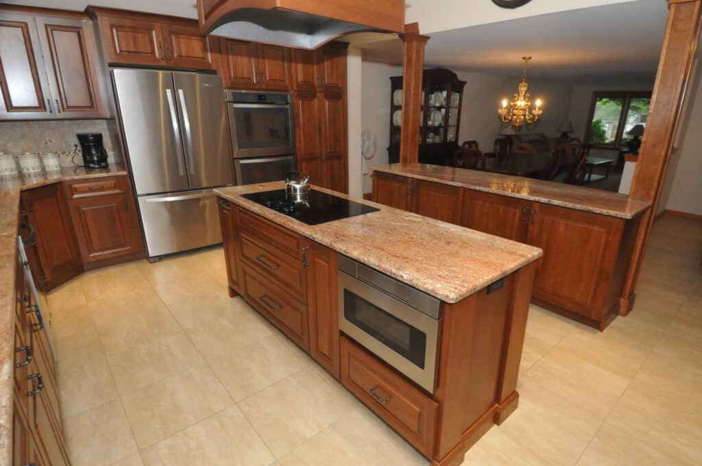 Spacious kitchen with wood cabinets, granite countertops, stainless steel appliances, a center island with a built-in microwave, and a view into a dining room with a chandelier.