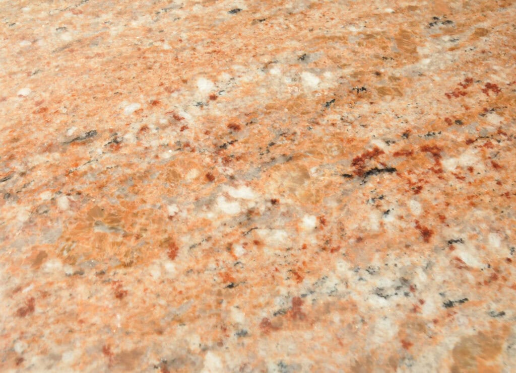 Close-up of a polished granite surface featuring a mix of warm orange, beige, white, and black specks and veins, creating a natural, textured pattern typical of stone countertops.