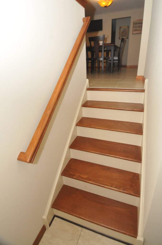 A small staircase with wooden steps and a handrail on the left leads up to a dining area with a table and chairs visible at the top. The walls are light-colored.