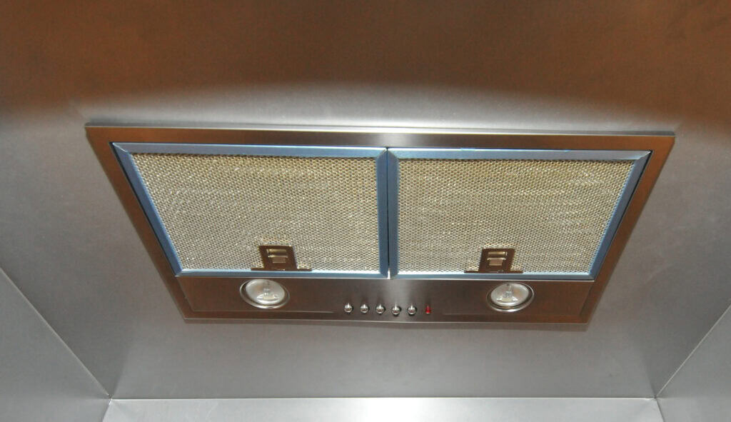 A stainless steel kitchen range hood with two mesh filters, two round lights, and a row of control buttons beneath the filters.