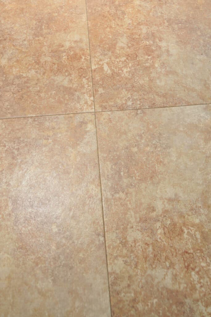 Four beige and light brown ceramic floor tiles with a subtle marbled pattern, arranged in a square grid with visible grout lines intersecting at the center.
